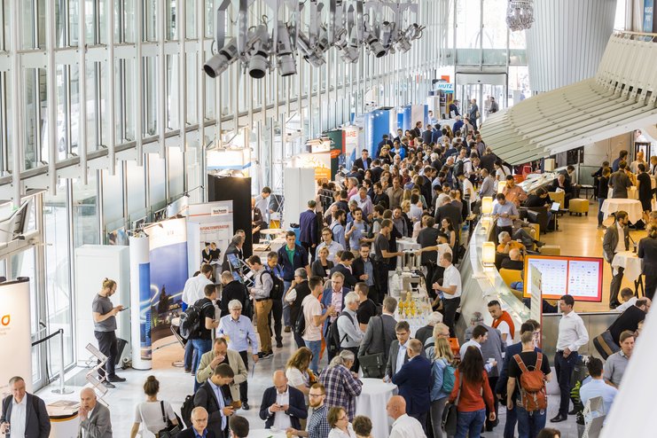 Das Bild zeigt aus der Vogelperspektive einen großen lichtdurchfluteten Saal mit vielen Fenstern. Unten ist ein Fluss aus Menschen zu sehen. 