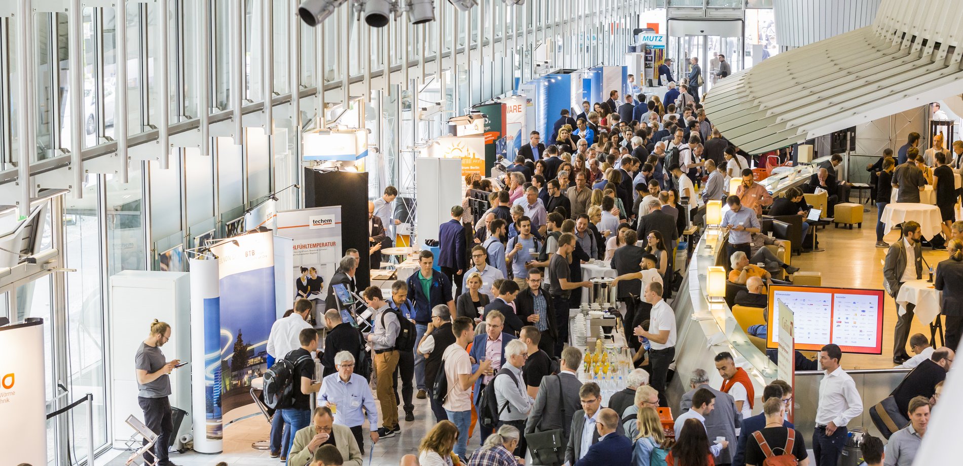 Das Bild zeigt aus der Vogelperspektive einen großen lichtdurchfluteten Saal mit vielen Fenstern. Unten ist ein Fluss aus Menschen zu sehen. 