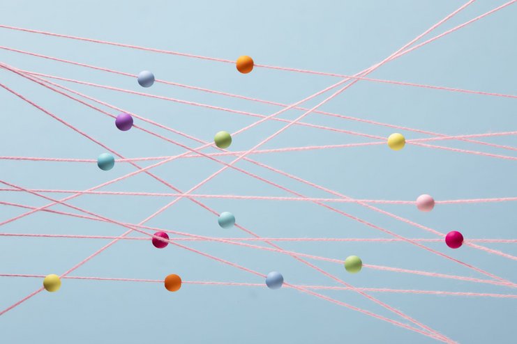 Pastellfarbene Perlen zufällig auf pinken Schnüren angeordnert, blauer Hintergrund