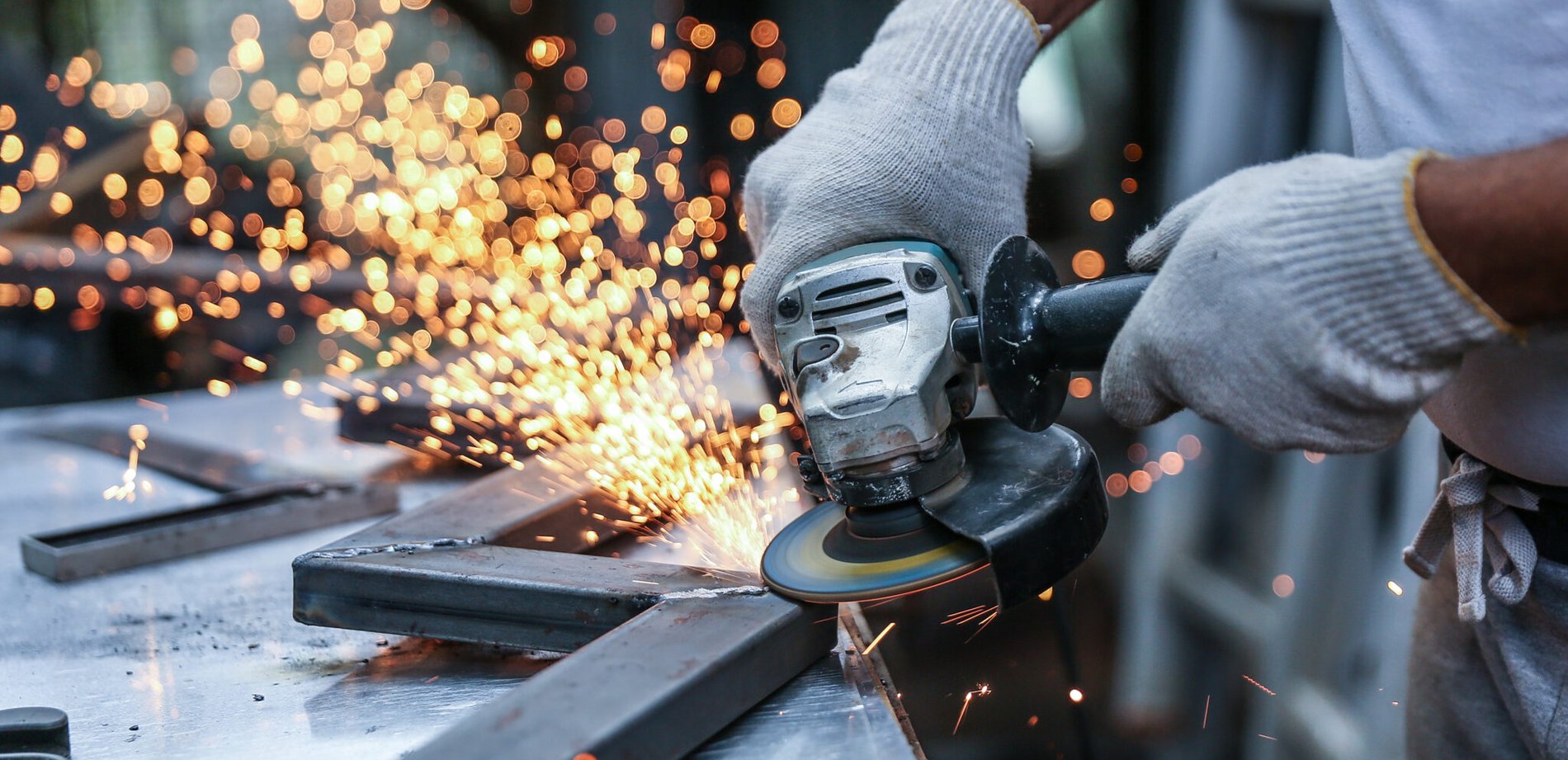 Nahaufnahme von Metallarbeiten in der Werkstatt: Die Hände eines Meisters sägen Metall mit einem Schleifgerät. 