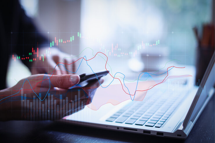 Doppelbelichtung: Handelswachstumsdiagramm auf Geschäft und Investition im Vordergrund, im Hintergrund ein Laptop und Smartphone, das gerade benutzt wird.