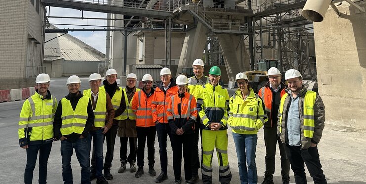 Gruppenfoto von Perosnen mit Bauhelmen und Warnwesten auf einem Industriehof.