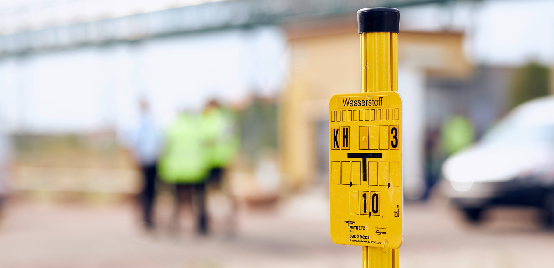 Gelbe Wasserstoff-Tafel vor Bauarbeitern im Hintergrund