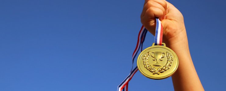 Hand, die eine Siegermedaille in den blauen Himmel streckt.