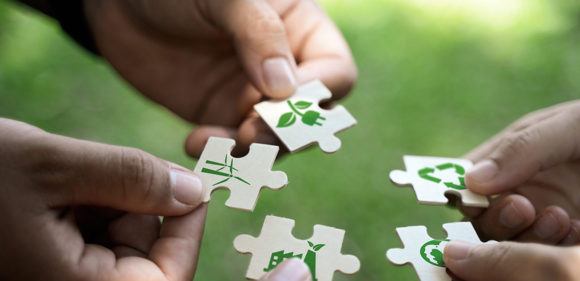 Fünf Hände halten Puzzleteile mit Nachhaltigkeitssymboles zum Thema Netto-Null und CO₂-Neutralität..