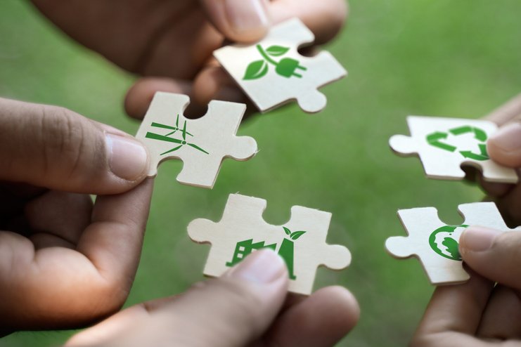 Hände halten Puzzleteile mit Nachhaltigkeitssymbolen