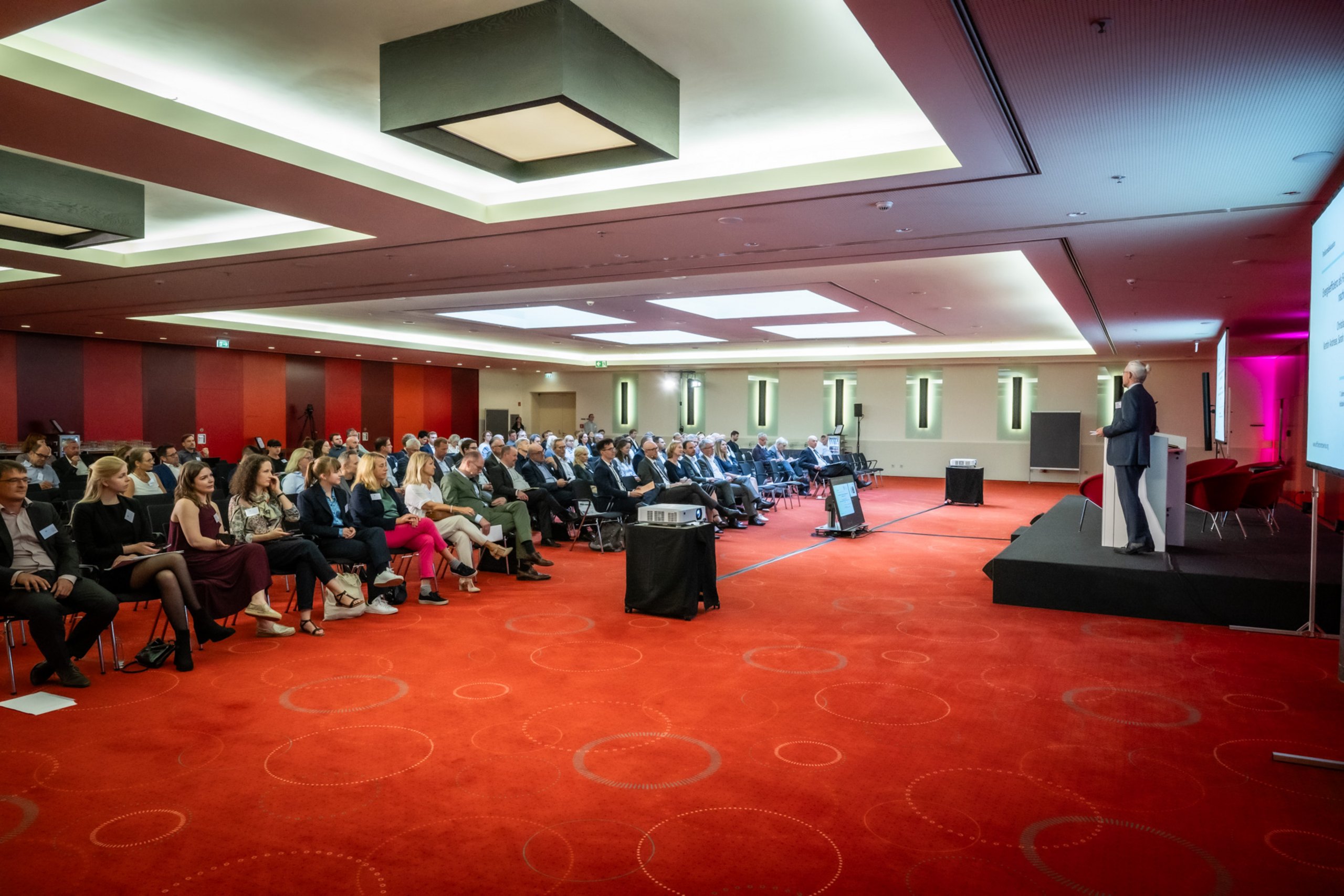 Podium mit Redner vor Publikum bei der Jahresveranstaltung 2023 der Netzwerkinitiative 