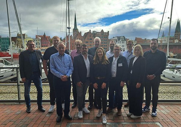 Das Bild zeigt die Mitglieder des Netzwerks in Lübeck vor einer maritimer Kulisse am Hafen. Im Hintergrund sind Segelschiffe zu sehen. 