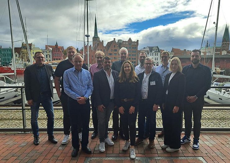 Das Bild zeigt die Mitglieder des Netzwerks in Lübeck vor einer maritimer Kulisse am Hafen. Im Hintergrund sind Segelschiffe zu sehen. 