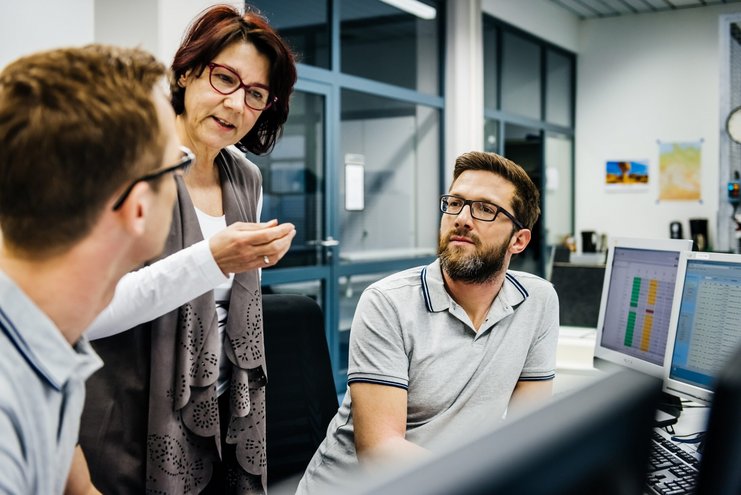 Geschäftsfrau spricht mit zwei Männern am Schreibtisch eines Kontrollraums.
