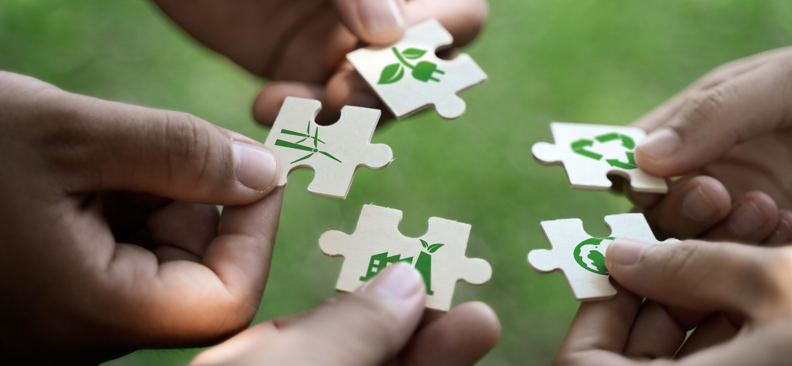 Hände halten Puzzleteile mit Nachhaltigkeitssymbolen